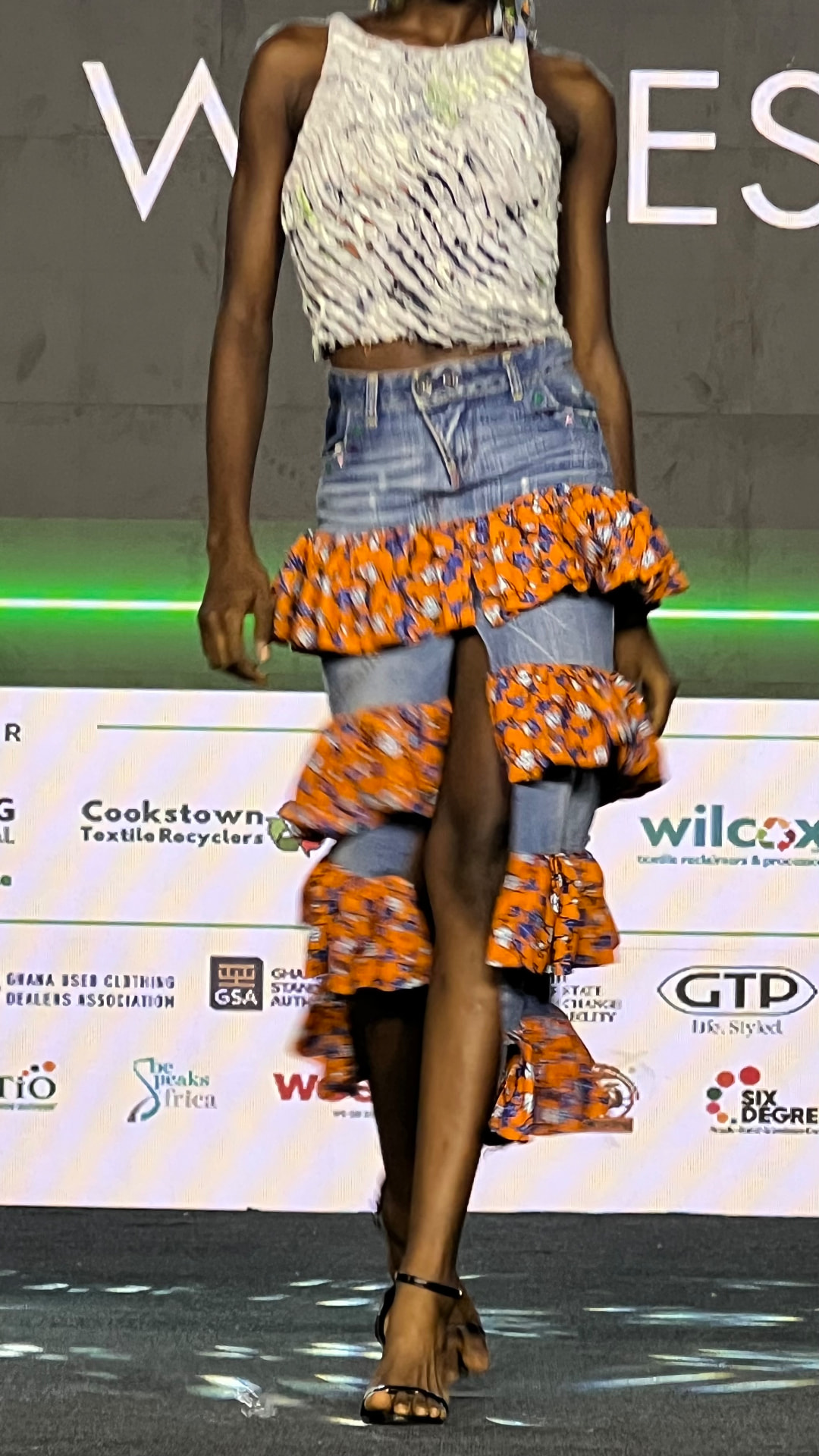Model on the L2L Summit runway wearing a denim skirt tiered with orange print ruffles from reclaimed cloth.