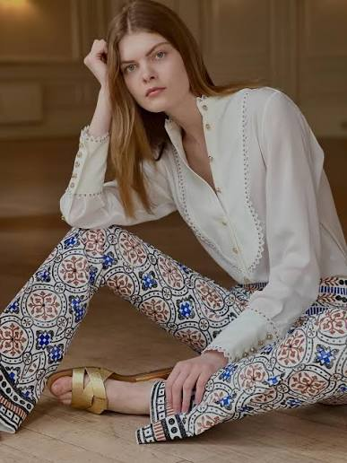 A model in a white blouse with tile-print trousers and gold sandals
