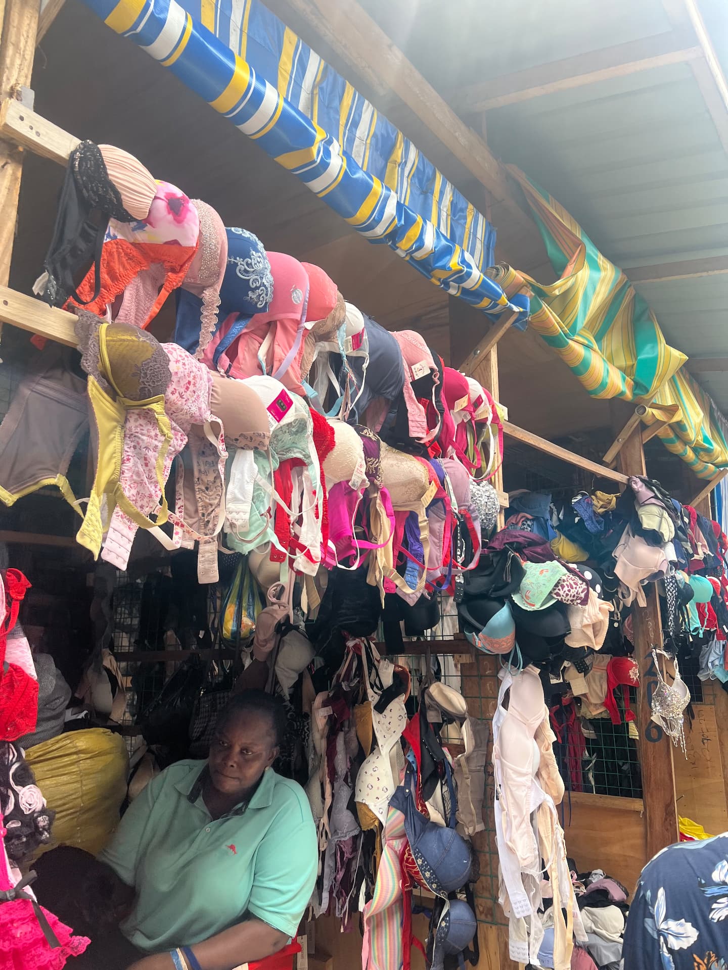A Kantamanto trader beneath a rack of second-hand bras hung from her stall.