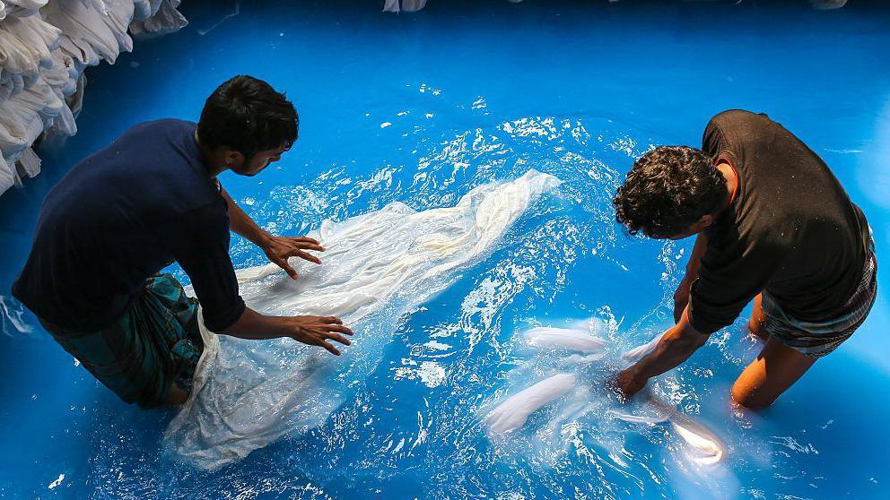 Workers wash and dye fabric by hand in a blue dyeing pool