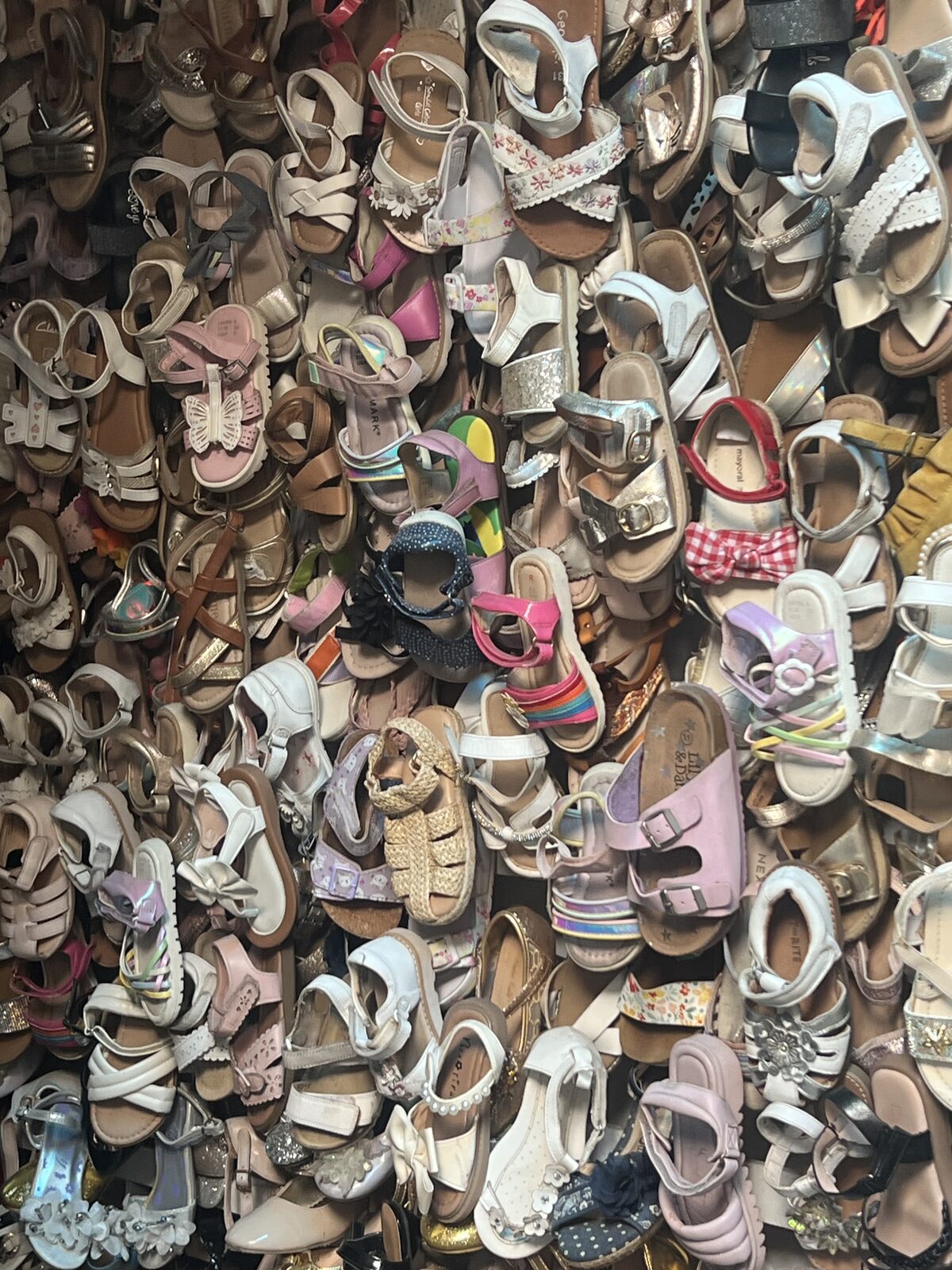 A dense wall of second-hand children's sandals and shoes for resale in a textile market