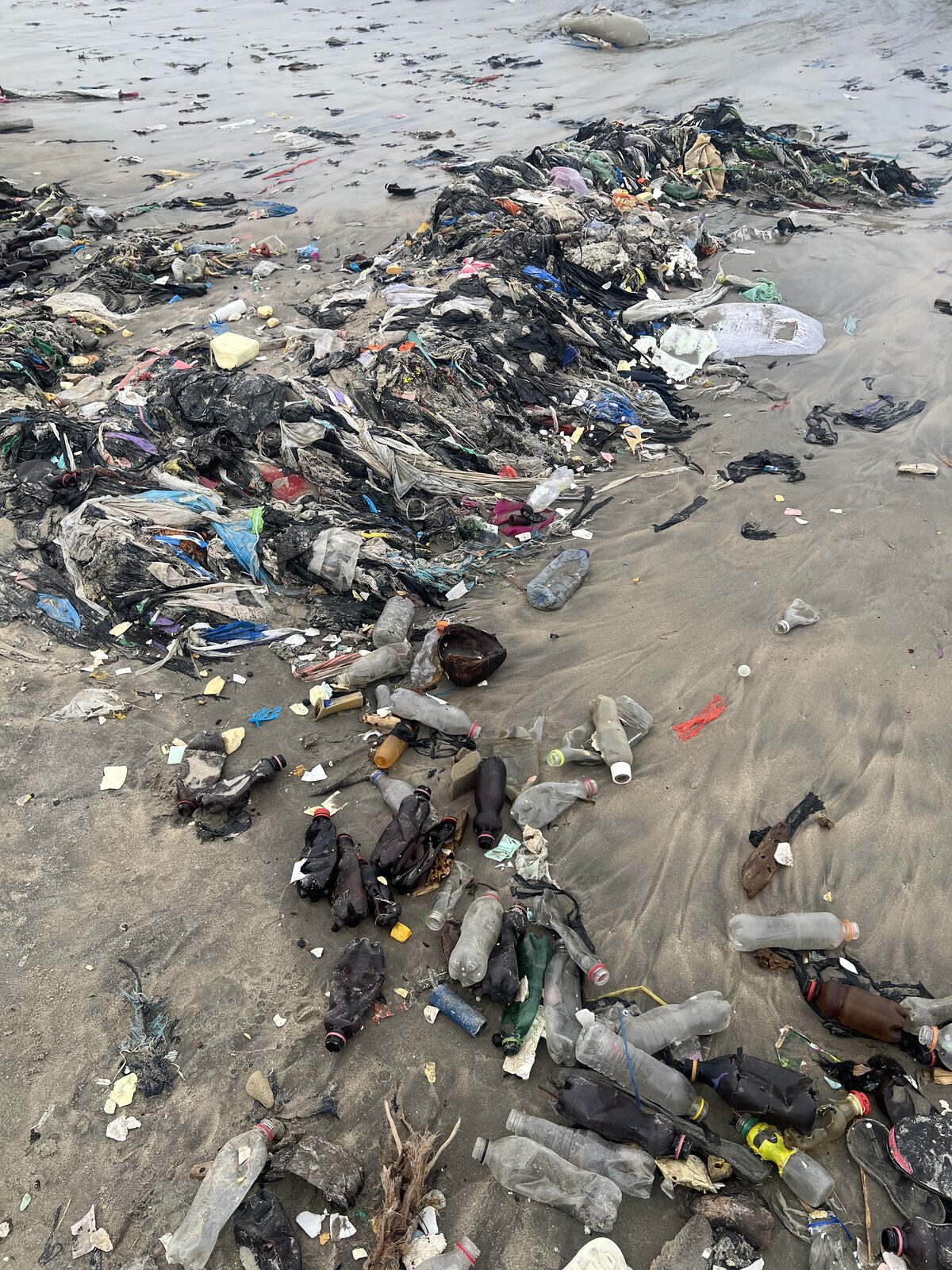 Textile and plastic waste washed up along a polluted shoreline in an emerging market